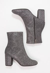 Szare botki za kostkę o błyszczącej teksturze, z wysokim słupkiem, spiczastym noskiem oraz detalem w postaci zapięcia na suwak z boku. Gładki materiał syntetyczny.