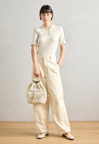 Polo shirt beige clair côtelé à manches courtes, associé à un pantalon ample crème et un sac à cordon assorti, complété par des ballerines beiges.