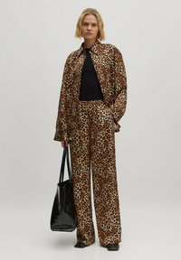 Jasje en broekset met luipaardprint in bruin en beige tinten; jasje heeft een oversized pasvorm, broeken zijn wijd gesneden; zwart topje en tas inbegrepen.