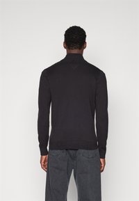 Czarny dzianinowy sweter z długimi rękawami i półgolfem. Fakturowana tkanina oraz prążkowane mankiety i dół. Detale w kształcie litery V z tyłu przy dekolcie.