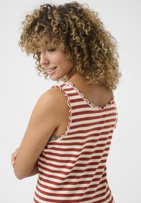 Top senza maniche a righe in rosso e crema con texture a coste e spalline con bordo scallop. Il retro presenta un design aderente e una silhouette rilassata.