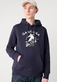 Sudadera con capucha azul marino, con un bolsillo tipo canguro en el frente, que presenta un gráfico de estilo vintage de un club de esquí en blanco y capucha con cordón.