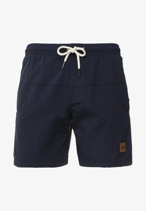 Pantaloni de baie bleumarin dintr-un material ușor, cu un brâu elastic și șnur, și o mică emblemă maro pe lateral.
