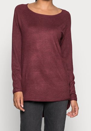 Weinrotes Langarmshirt mit weitem Ausschnitt, gerippter Textur und einem leicht verlängerten Rückensaum, kombiniert mit dunkelgrauen Jeans.