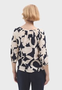 Námořnická a krémová vzorovaná blůza s tříčtvrtečními rukávy a nařaseným výstřihem. Tkanina se zdá být lehká s mírně texturovaným povrchem.