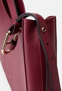 Borsa in pelle bordeaux con una finitura testurizzata, dotata di una chiusura in metallo dorato e di una tracolla regolabile con dettagli di cucitura.