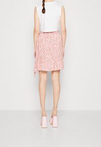 Gonna rosa a fiori con un orlo a balze e un laccio laterale, abbinata a scarpe con tacco a blocco rosa chiaro. Top senza maniche bianco minimalista.