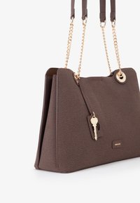 Borsa a tracolla marrone con texture, dotata di spalline in catena dorata, un accento a forma di chiave e un bordo inferiore liscio. Presenta un design strutturato e un dettaglio con il logo.