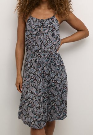 Vrouw draagt een mouwloze, knielange jurk met dunne bandjes en een zwart paisley-patroon met blauwe en roze accenten.