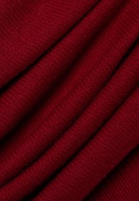 Czerwony dzianinowy materiał o teksturowanej powierzchni i prążkowanym wzorze, wyeksponowany w nakładających się fałdach. Miękki, ciepły i gęsto tkany.