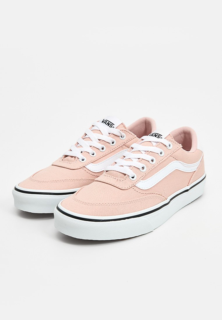 Zapatillas de lona de color rosa claro con cordones blancos, una franja lateral blanca y detalles negros en la suela, con una punta redondeada y diseño de caña baja.