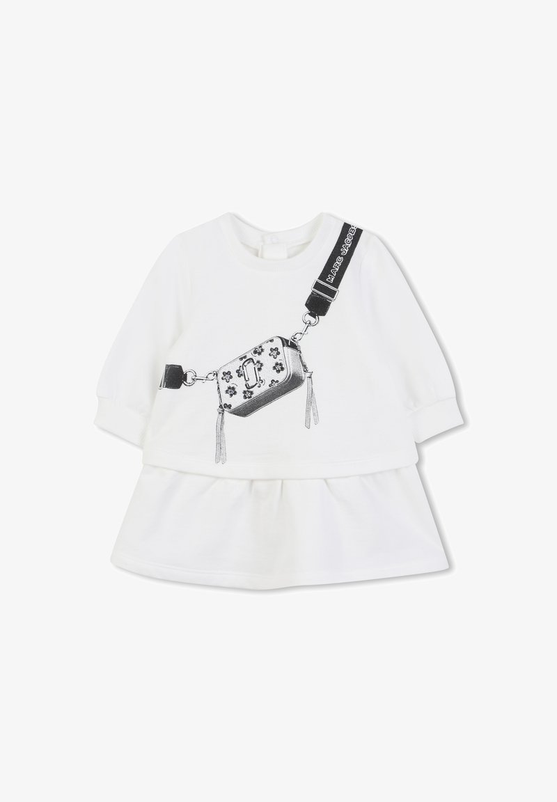 Robe pour bébé à manches longues blanche avec un sac bandoulière noir imprimé et des détails de sangle à l'avant, ornée de décorations florales et de texte sur la sangle.