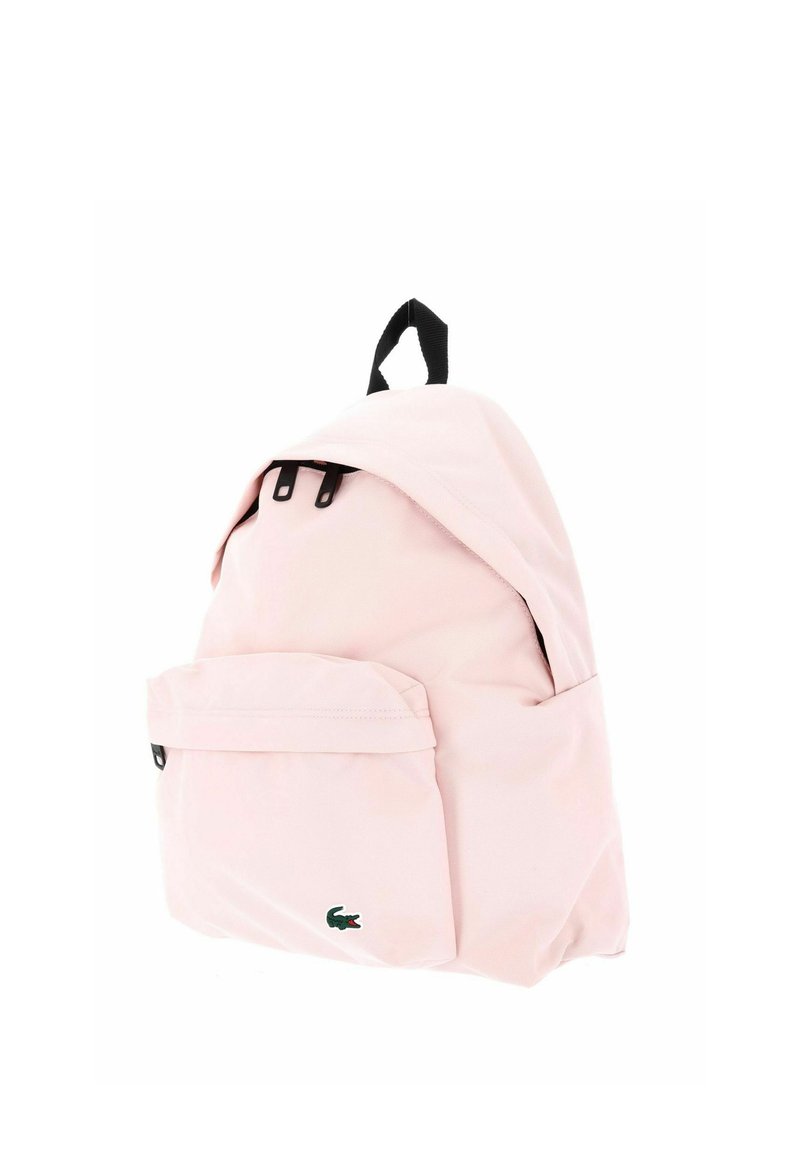 Light pink backpack with a front pocket, black zipper pull tabs, black top handle, and a small green crocodile logo on the front pocket.