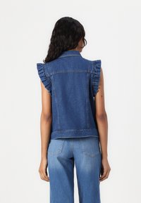 Denimvest med volangerm, lys vask, tettsittende design, ryggsøm, og to lommer. Kombinert med matchende vide blå jeans.