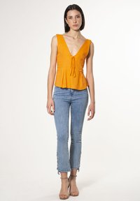Top peplum arancione con scollatura a V e dettaglio con cordino, abbinato a jeans skinny azzurri chiari con orli a spacco e decorazioni alle caviglie.