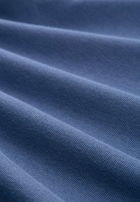 Weicher blauer Stoff mit strukturierter Rippenstruktur, der mehrere Falten und sanfte Knicke zeigt und seine glatte Oberfläche sowie die gleichmäßige Farbe betont.