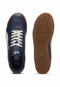 Námořnické a bílé tenisky Puma s bílými tkaničkami, viditelným vzorem podrážky a gumovou podešví, zobrazené z horního a spodního pohledu.