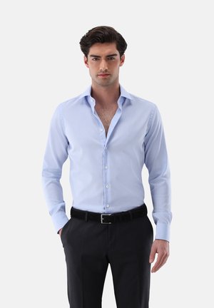 Hellblaues Langarmhemd mit einem Button-Down-Kragen, glatter Textur und weißen Knöpfen, kombiniert mit dunklen Hosen und einem schwarzen Gürtel.