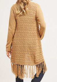 Sweter kardigan w jasnobrązowym kolorze z falistym wzorem, długimi rękawami i frędzlami na dole. Wykonany z miękkiego materiału, o luźnym kroju.