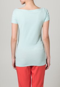 Hellblaues kurzärmeliges Top mit U-Boot-Ausschnitt, glatter Textur, kombiniert mit korallenfarbenen Hosen, die eine figurbetonte Silhouette und eine Tunika-Länge zeigen.