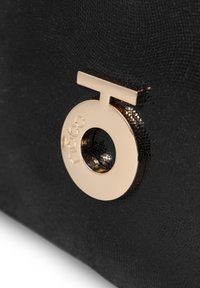 Borsa nera in tessuto con un accento in metallo dorato a forma circolare con un centro a taglio e dettagli del logo impresso.