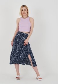 Marinblå blommig kjol med en sidofåra, parat med en ljuslila kort ärmad topp. Texturerat tyg visas med minimalistiska sandaler.