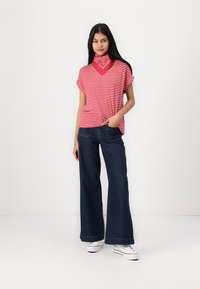 Haut à rayures rouges et blanches à manches courtes avec décolleté en V, associé à un jean large bleu foncé et des baskets blanches, rehaussé par un bandana rouge.