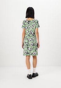 Rochie florală verde cu mâneci scurte, cu modele de flori alb-negru, croială până la genunchi, purtată cu pantofi masivi negri și șosete albe.