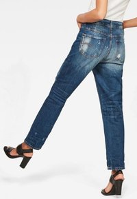 Blue denim jeans with a relaxed fit, distressed details, five-pocket design, and medium wash. Pairing with black high-heeled sandals.