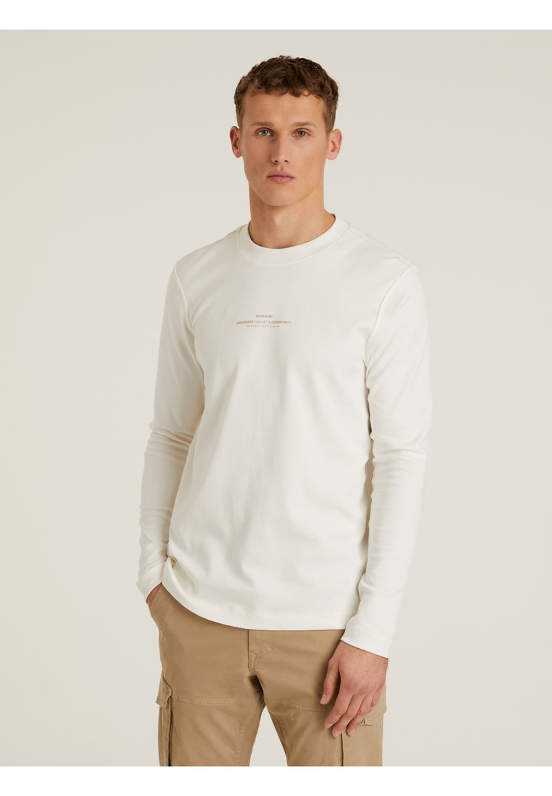 Weiße langärmelige T-Shirt aus Baumwolle mit Rundhalsausschnitt und kleinen bedruckten Text auf der Vorderseite. Getragen mit beigen Cargo-Hosen.