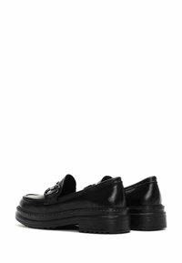 Mocasines de cuero negro con un tacón bajo, que cuentan con una hebilla decorativa y una textura suave. Punta redondeada y suela de goma resistente.