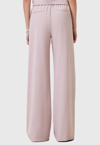 Lichtroze wijde broek gemaakt van soepel materiaal, met een elastische tailleband en twee achterzakken. Eenvoudig, elegant ontwerp.