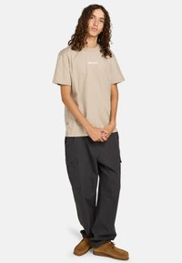 Beige bavlněné tričko s logem "element" v kombinaci s tmavě šedými cargo kalhotami. Hnědé boty dotváří outfit. Neformální a uvolněný střih.