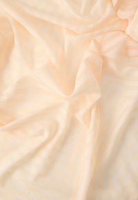 Tissu beige doux avec des motifs rayés et géométriques subtils, légèrement froissé et plié, créant des variations de lumière et d'ombre.