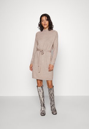Beige knitted dress with a high neckline and a waist tie, featuring long sleeves. Paired with knee-high striped boots in black and white.