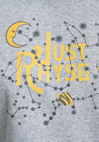 Szürke pulóver grafikus nyomattal, amelyen sárga szöveg olvasható: "Just Rhyse", egy félhold, csillagok és csíkos bolygó dizájn található.