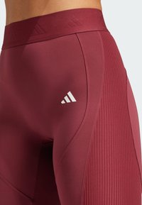 Burgunderfarvede atletiske leggings med ribbet tekstur og glat overflade, der har et hvidt logo på låret og en bred, elastisk talje.