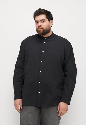 Camisa negra de manga larga con cuello abotonado, que presenta botones blancos y una textura suave, combinada con pantalones grises texturizados.
