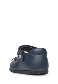Námořnická modrá kožená obuv s kulatou špičkou, nastavitelným popruhem a detailním stříbrným knoflíkem. Hladká textura a nízký podpatek.