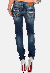 Jeans skinny blu scuro con un design sbiadito, due tasche posteriori con cuciture chiare, abbinati a scarpe con tacco alto argento dotate di borchie.