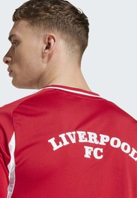 Ung man med kort hår iklädd en röd Liverpool FC sporttröja, sedd från ryggen och vänd något åt sidan.