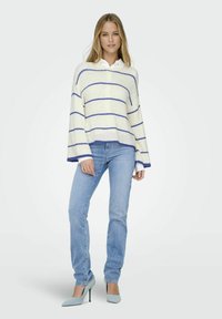 Sweter w paski w kolorze kremowym z niebieskimi liniami, luźny krój i szerokie rękawy, zestawiony z jasnoniebieskimi dżinsami oraz jasnoniebieskimi czółenkami.