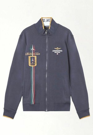 Giacca navy con zip e colletto alto, foderata in giallo, con strisce tricolori italiane e ricamo "Aerobatic Team" e insegna sul davanti.