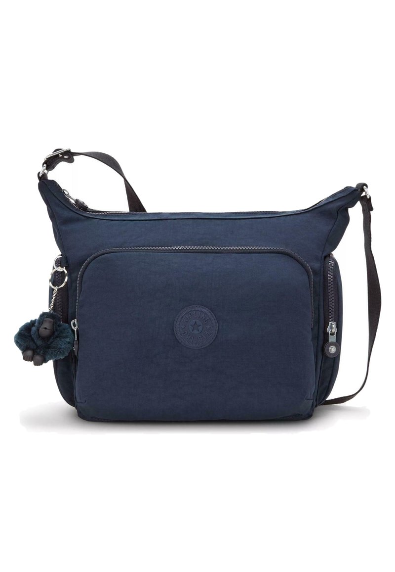 Borsa a spalla in tessuto navy con tasca frontale con zip, esterno textured e logo circolare. È attaccato un portachiavi a forma di scimmietta in peluche.