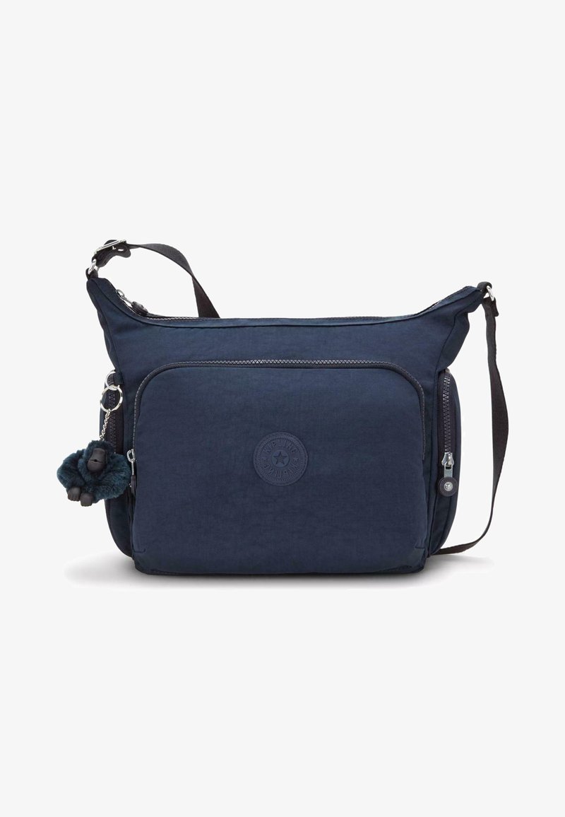 Navy fabric shoulder bag with a front zipper pocket, textured exterior, and circular logo. Attached is a plush monkey keychain.