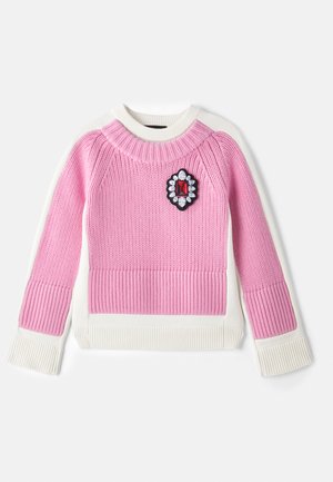 Pulover tricotat roz cu o textură ribbed, manșete și tiv ribbed albe, și o broșă decorativă cu o piatră roșie și cristale transparente.