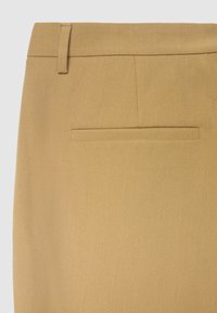 Pantalon beige sur mesure avec une texture lisse, une coupe slim et une poche arrière unique avec un design de passepoil discret.