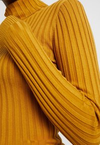 Ribbad polokragetröja i senapsgul. Fitted design med förlängda ärmar och vertikala ribbor för textur.