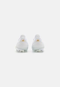 Valkoiset urheilukengät, joissa on sileä synteettinen päällinen, kultaiset yksityiskohdat ja läpinäkyvä pohja. Pyöristetty kantapää, jossa on tekstuuripintoja.