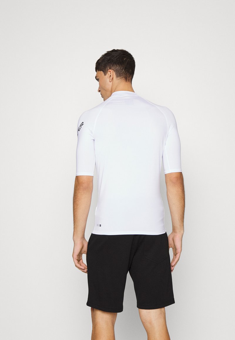 White fitted short-sleeve surf shirt with seamless design, worn with black shorts. Features a logo on the left shoulder. Smooth texture.